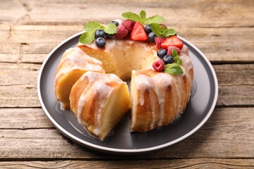 Pieces of delicious bundt cake with berries, glaze and mint on wooden table, closeup