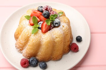 Delicious bundt cake with powdered sugar, berries and mint on pink wooden table, closeup