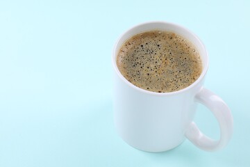 Aromatic coffee in cup on light turquoise background, closeup. Space for text