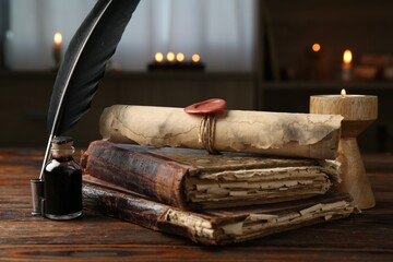 Old rolled scroll, burning candle, feather, inkwell and books on wooden table, closeup