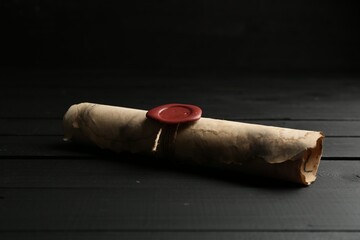 One old rolled scroll with wax seal on black wooden table, closeup