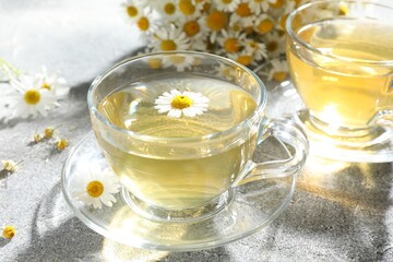 Tasty chamomile tea and flowers on light grey table, closeup