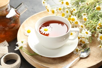 Tasty chamomile tea and flowers on black table, closeup