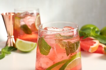 Tasty cocktail with ice cubes, lime and grapefruit on white table, closeup