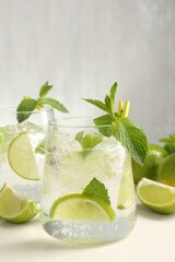 Tasty cocktail with lime and ice cubes on white table, closeup