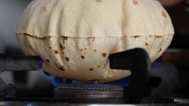 Close up shot of cooking a wheat roti or chappati being roasted puffed and swollen on a blue gas flame in the kitchen.