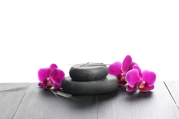 Acupuncture needles, orchid flowers and spa stones on grey wooden table against white background