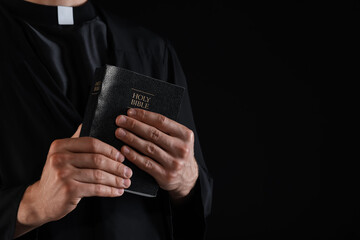 Priest with Holy Bible on black background, closeup. Space for text