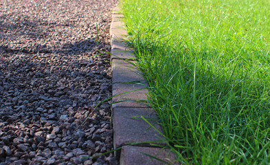 Morning dew on fresh grass of the lawn near an accurate gravel path with shadow from the trees. Separation of walking and recreation areas of a private yard  
