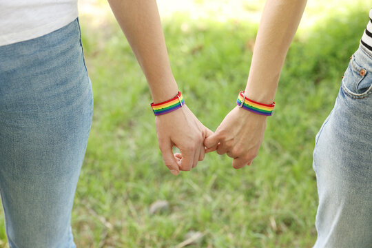 LGBT concept. Women in rainbow wristbands holding hands outdoors, closeup