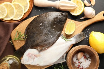 Fresh raw flounder fish, spices and juicer on black wooden table, flat lay. Seafood