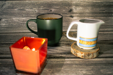 Dark green and white mugs with coffee on rustic wood, accompanied by a glowing red candle. Warm, cozy, and inviting scene perfect for lifestyle and coffee concepts.