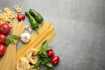 Different types of raw pasta and products on grey textured table, flat lay. Space for text