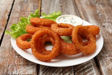 Fried squid rings served with sauce on wooden table, closeup