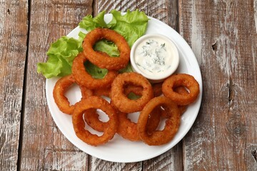 Fried squid rings served with sauce on wooden table, top view