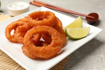 Fried squid rings, lime, sauce and chopsticks on grey table, closeup