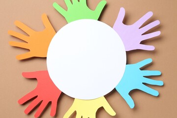 Tolerance concept. Colorful paper hands and empty card on brown background, top view. Space for text