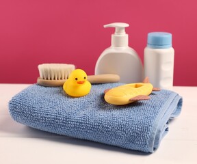 Baby accessories and bathing products on white wooden table against pink background