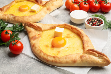 Tasty khachapuri with cheese, egg and other products on light grey background, closeup