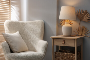 Stylish wooden side table with lamp near armchair at home