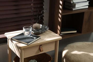 Wooden side table with glass of water, notebook and air reed diffuser indoors
