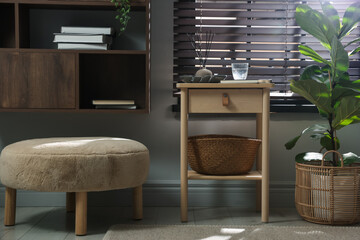 Wooden side table with glass of water, notebook, air reed diffuser and basket near window indoors