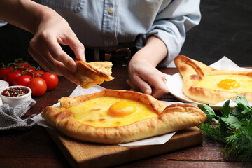 Woman eating delicious khachapuri at wooden table, closeup