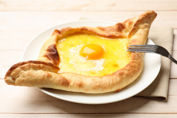 Tasty khachapuri with cheese, egg and fork on wooden table, closeup