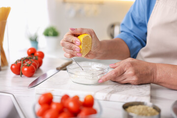 Senior woman cooking at white marble table in kitchen, closeup