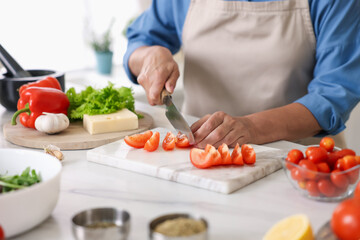 Senior woman cooking at white marble table in kitchen, closeup