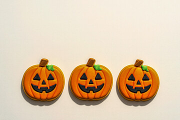 Obraz premium Three festive jack-o’-lantern shaped pumpkin cookies decorated with orange and black icing, arranged in a row on a light background, fun and colorful Halloween holiday treat perfect for food photo