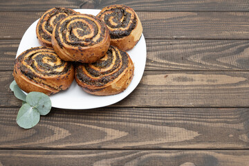 Close-up of spiral poppy seed rolls on wooden table. Homemade pastry dessert with rich filling, arranged on a plate with leaves. Perfect for bakery promotion, cafe menus, food blogs, and recipe ideas