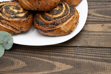 Close-up of spiral poppy seed rolls on wooden table. Homemade pastry dessert with rich filling, arranged on a plate with leaves. Perfect for bakery promotion, cafe menus, food blogs, and recipe ideas