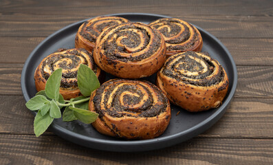 Close-up of homemade poppy seed rolls on a plate over wooden table. Golden brown pastry swirls filled with rich poppy seed filling. Concept of homemade baking, sweet pastry, desserts and bakery food