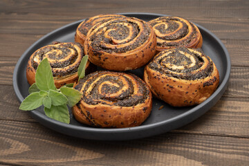 Close-up of homemade poppy seed rolls on a plate over wooden table. Golden brown pastry swirls...