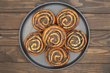 Close-up of homemade poppy seed rolls on a plate over wooden table. Golden brown pastry swirls...