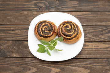 Close-up of spiral poppy seed rolls on wooden table. Homemade pastry dessert with rich filling, arranged on a plate with leaves. Perfect for bakery promotion, cafe menus, food blogs, and recipe ideas