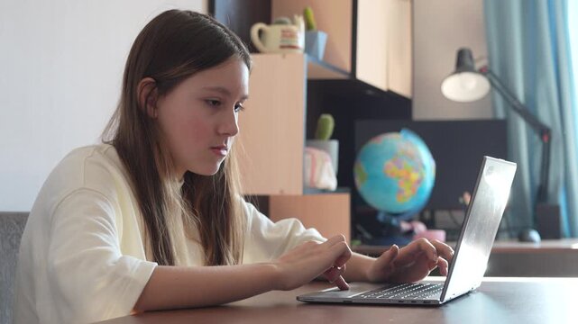 Girl is using a laptop for education. girl is studying remotely at home. girl in a white blouse is doing her homework on laptop. student was tired in remote lesson. schoolgirl sitting at a table.