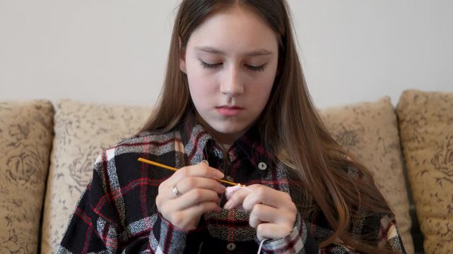 Young girl in warm sweater knitting on sofa at home. Space for text