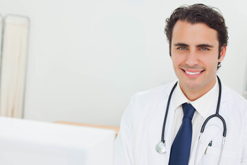 Mid adult male physician standing in examination room with white coat and stethoscope, copy space