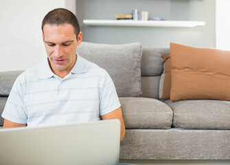 Mid adult male working on silver laptop while sitting on floor in living room, copy space