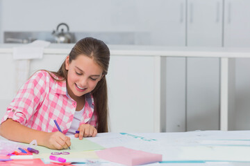Girl aged ten sitting at home kitchen table drawing on green paper with markers, copy space