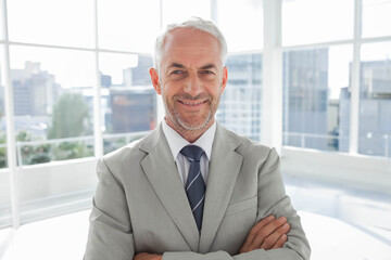 Senior businessman standing in suit and striped tie in office with windows overlooking skyline