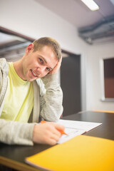 Man studying at classroom desk holding orange pencil above notebook near yellow folder, copy space