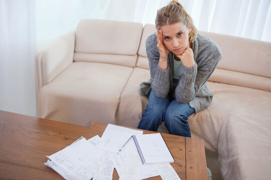 Woman sitting on sofa while reviewing receipts on coffee table in living room, copy space