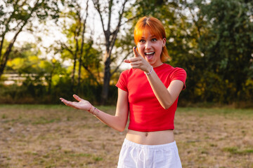 Excited young woman pointing and showing with open hand in park