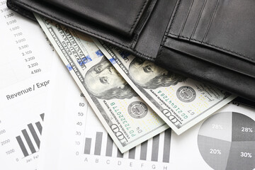 Black leather wallet with dollar bills. Cash money on financial report papers. Business charts and...