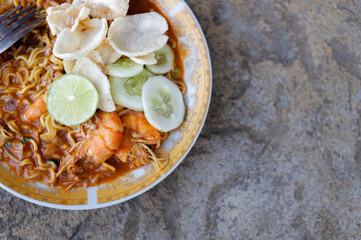Spicy stir-fried shrimp instant noodles seafood on white plate on stone, close-up with copy space