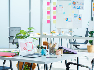 Modern office desk with laptop, colorful charts, sticky notes, and piggy banks, representing financial planning, business strategy, and workplace creativity in professional environment.

