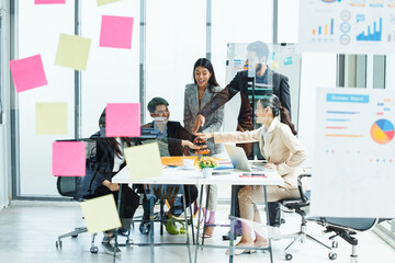 Group of Asian business professionals discussing project strategy in modern office with charts and whiteboard, symbolizing teamwork, corporate planning, and collaborative success.